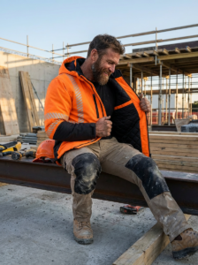 OAKLINE The Kimi Hi Vis Jacket In Orange - construction worker sat on steel beam on site